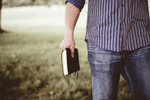 a man walking through a field carrying a Bible 