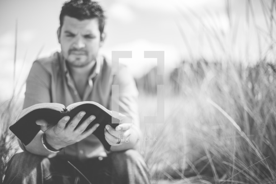 man reading the Bible sitting on a beach 
