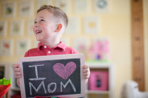 A little boy holding a chalkboard sign that reads I heart mom 