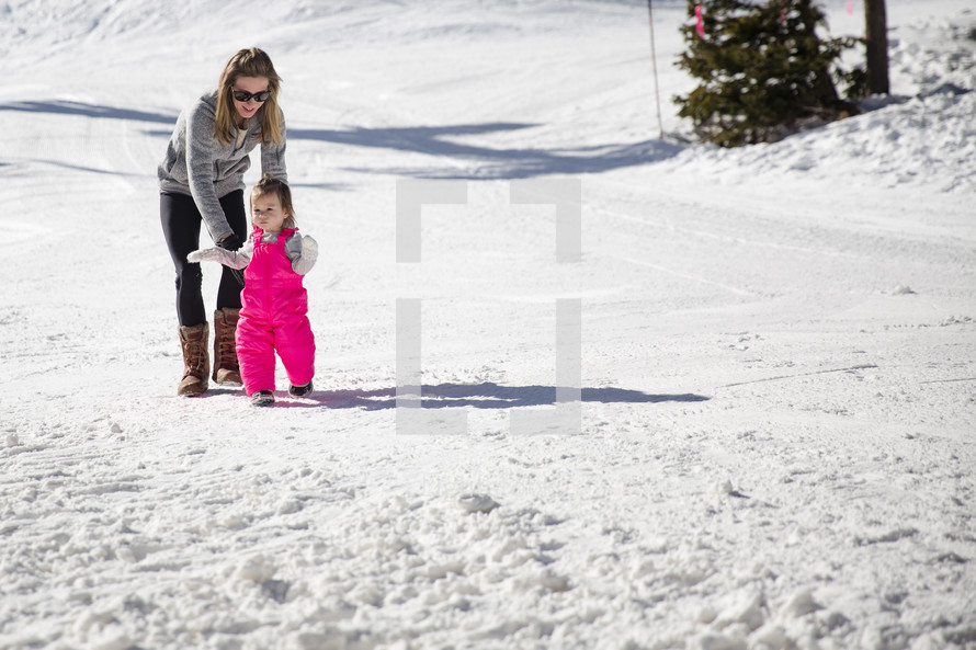 a mother and her toddler daughter playing in snow 