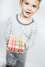 little boy in pajamas holding a gift 