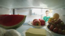 POV shot from inside a refrigerator of boy opening the door and taking out food