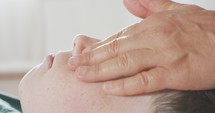 Shiatsu treatment. Masseuse giving a gentle face massage to a young boy