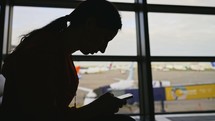 Businesswoman at airport with phone in hands against the large panoramic window with parking airplanes. Full-length girl stand in wait room boarding flight. Trip for business meet in another country.