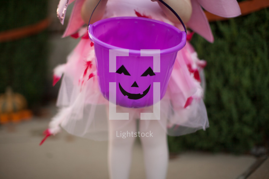 a little girl in a flamingo Halloween costume holding a candy bucket 