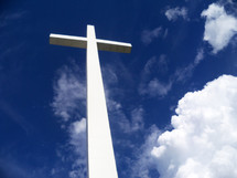 A large white cross stretches out against a blue sky surrounded by clouds and the earth's atmosphere as it stretches out between Heaven and Earth to show the power and reach of the gospel message to all the earth that Jesus was crucified, died then resurrected from the dead three days later overcoming the grave, death and sin for all of mankind for all ages. 