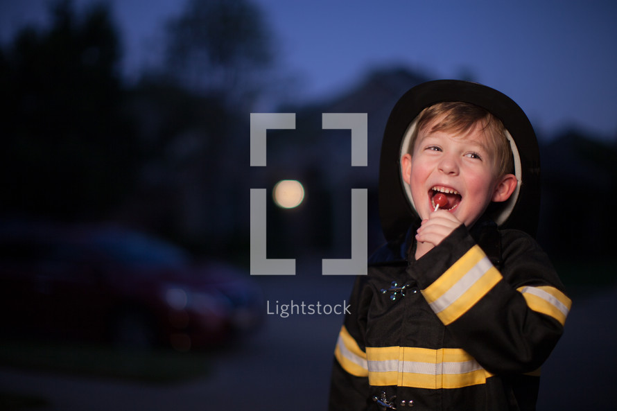 a boy in a fire fighter Halloween costume eating candy 