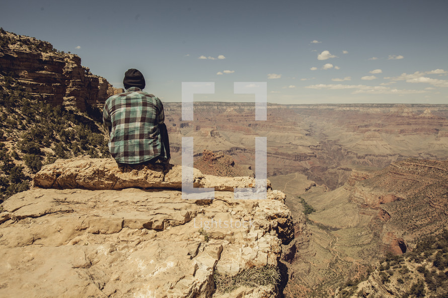 Man sitting on the edge of a rocky cliff looking down into the canyon.