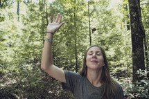 woman alone in a forest with hand raised 