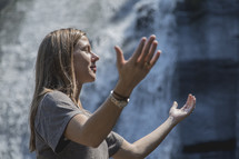 raised hands in worship in front of a waterfall 