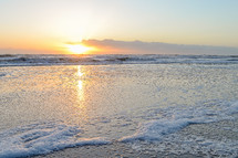 Foaming waves on beach at sunrise