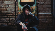 man with tattooed coffee sitting on a curb drinking coffee 
