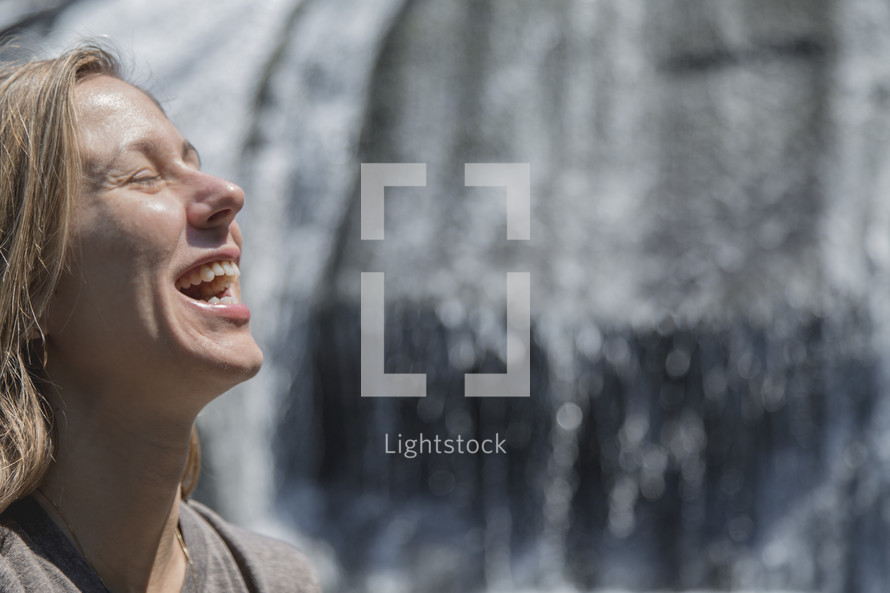 face of a joyful woman in front of a waterfall 