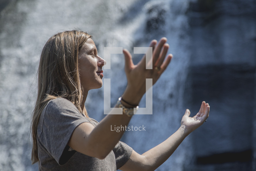 raised hands in worship in front of a waterfall 
