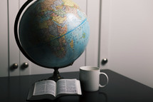 globe, open Bible, coffee mug on a desk 