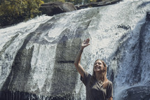 raised hand in front of a waterfall 