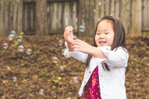 a girl child blowing bubbles outdoors 