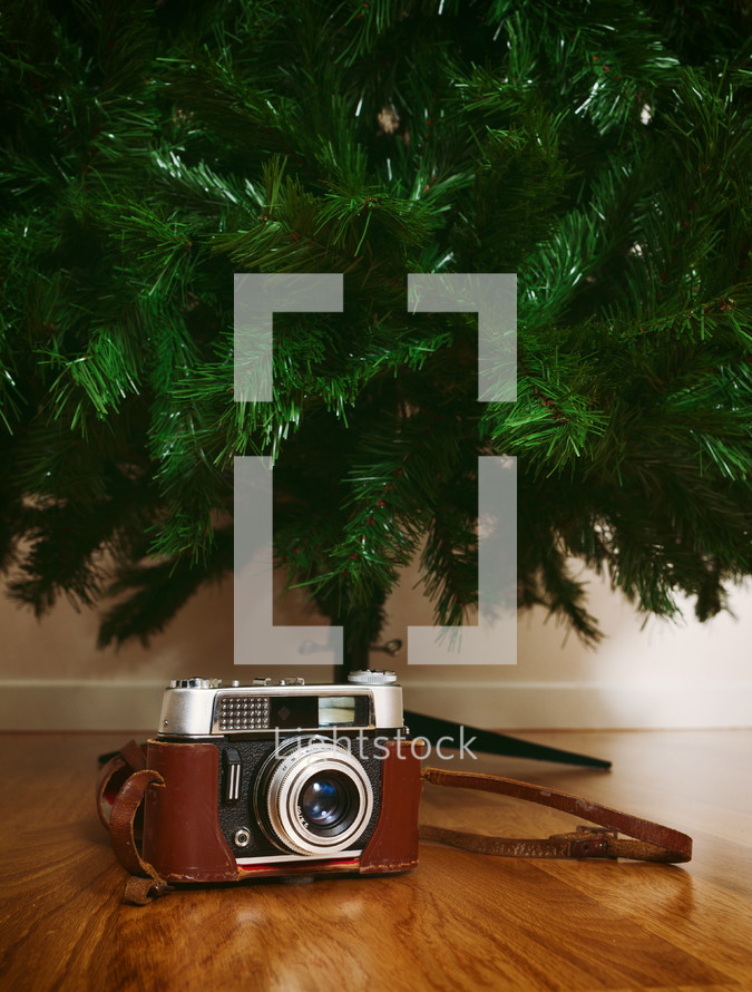 Vintage camera under bare artificial christmas tree on oak parquet flooring