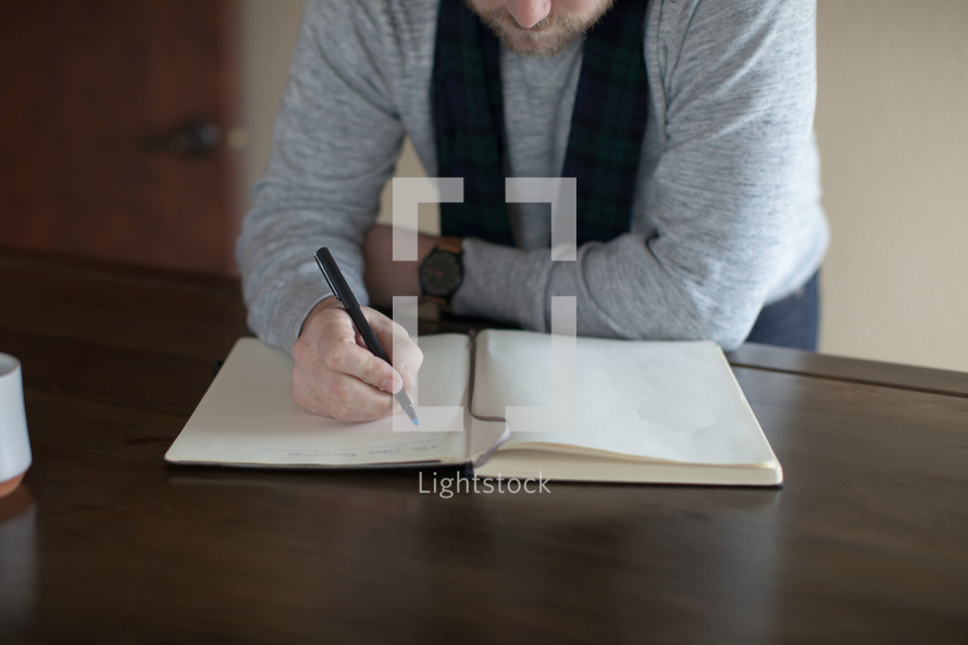 a man writing his New Year's resolutions in a journal 