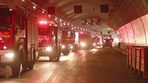 Fire trucks entering a large tunnel with red lights for rescue