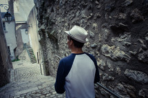 A man with a hat walks down some stone steps in an old town