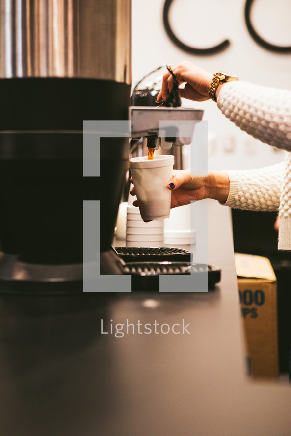 A woman getting a cup of coffee from a coffee machine.