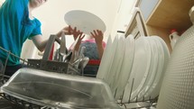 Little girl helping her mother fill the dishwasher with dirty dishes
