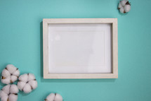 Blank white frame on turquoise background with cotton