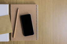 pencil, notebook, and cellphone on a wood table 
