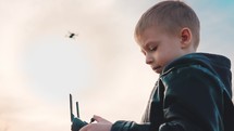 Happy boy plays with a drone in nature. Child controls the drone using a remote control.