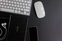 Bible, cross, tablet, earbuds, cellphone and mouse on a table 