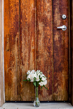 vase of flowers in front of a brown wood door 