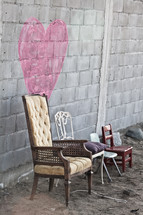 Pink heart painted on a stone wall of a building with several different kinds of chairs placed in front of the wall