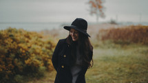 a young woman in a coat and hat standing on a shore at fall 