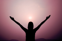 silhouette with raised hands and purple sky 