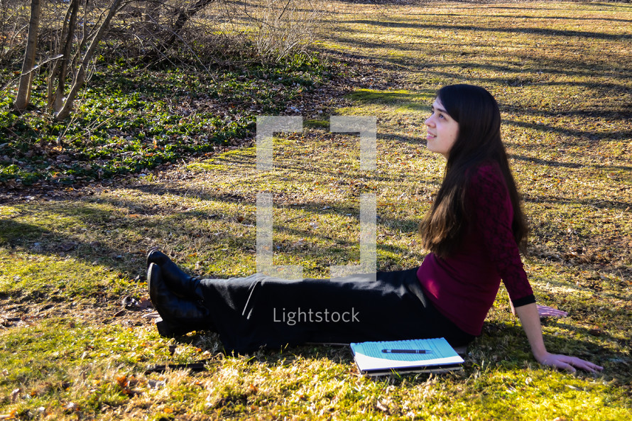 a girl sitting in warm sunlight with a notebook 
