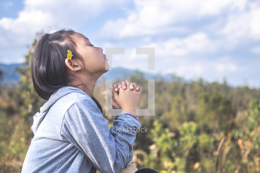 a little girl looking up to God and praying outdoors 
