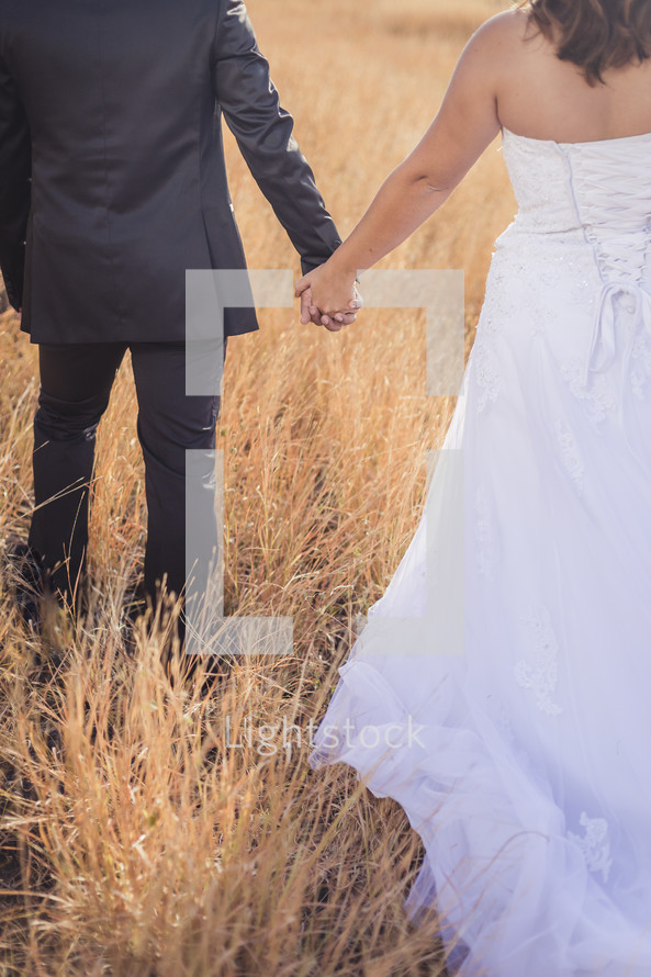 bride and groom walking through a field 