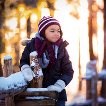 a boy leaning on a fence with snow 