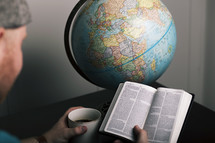 a man reading a Bible, holding a coffee mug, and globe 