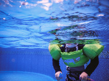 A child swimming in a pool wearing a lifejacket.