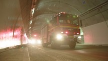Fire trucks entering a large tunnel with red lights for rescue