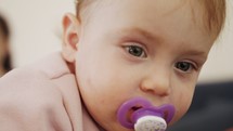 Cute baby girl playing at home with a pacifier in her mouth