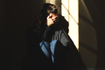 a crying woman sitting in a dark room covering her face 