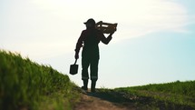 Silhouette of farmer carries shovel and wooden box. Farmer with a shovel walking on the field. On the Sunset.