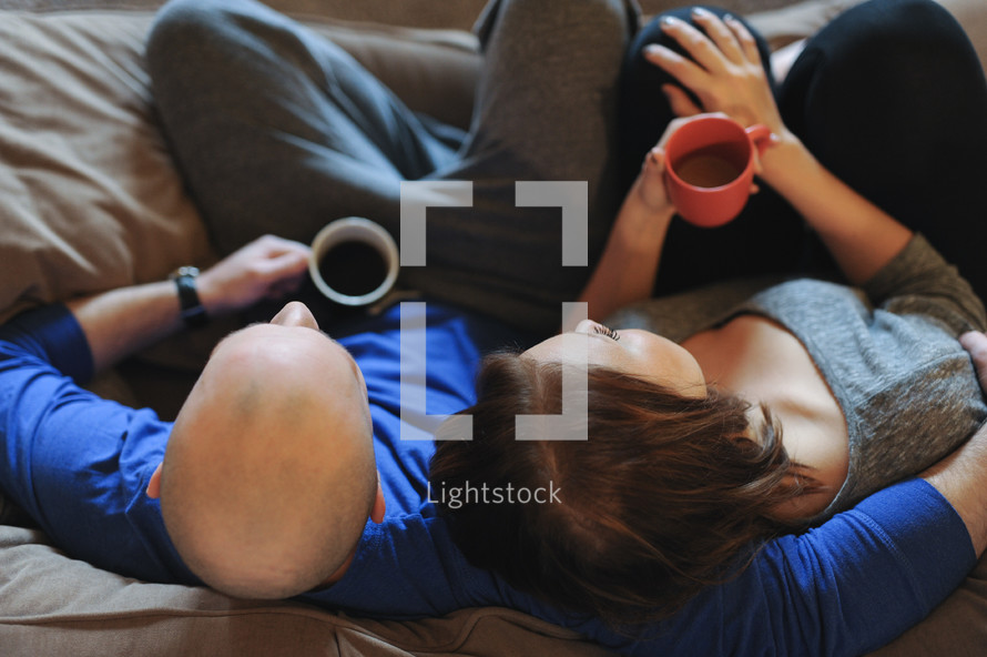 a couple snuggling on a couch holding coffee mugs 