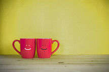 two red mugs with smiley faces 
