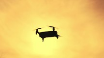 Drone copter flying during sunset. Modern technology and UAV concept. Quadcopter drone silhouette hovering and flying at sunset with a yellow sky.
