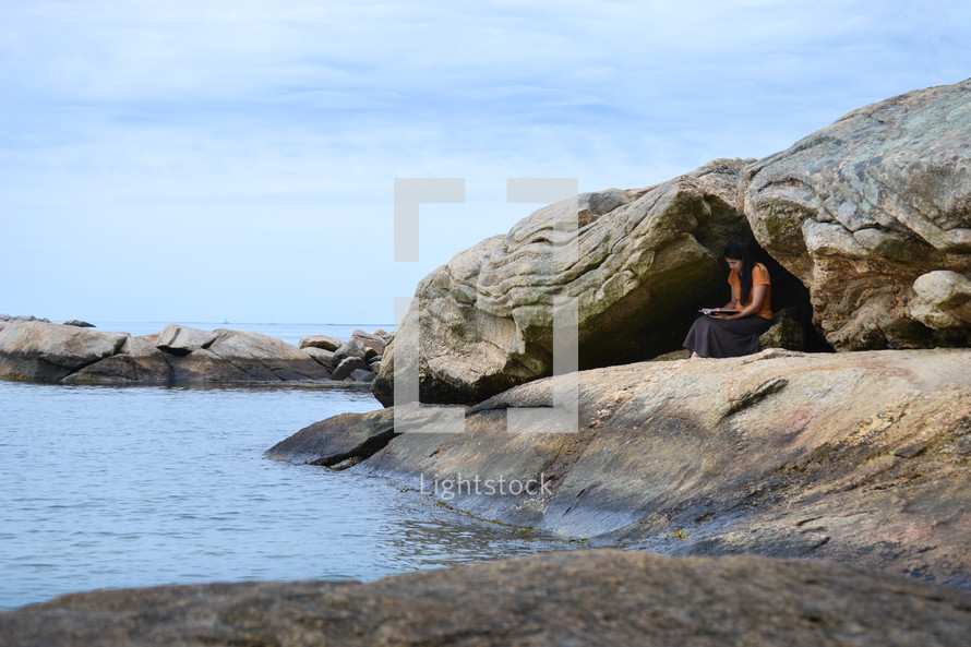 a woman reading a Bible on a rocky shore 