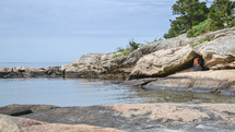 a woman reading a Bible on a rocky shore (wide)